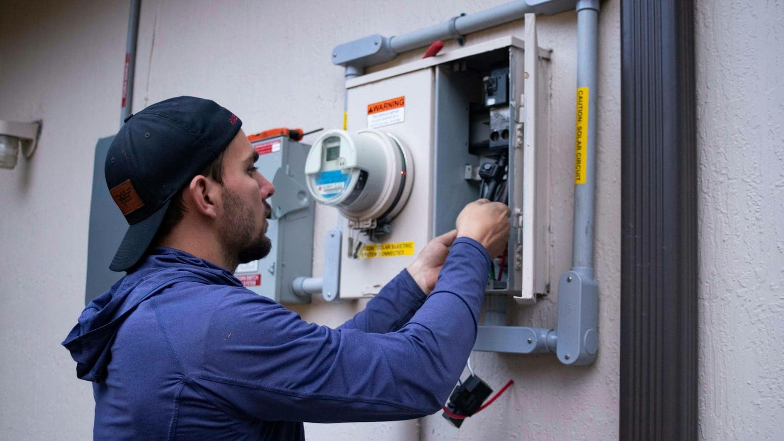 An electrician working on the electric meter outside a house