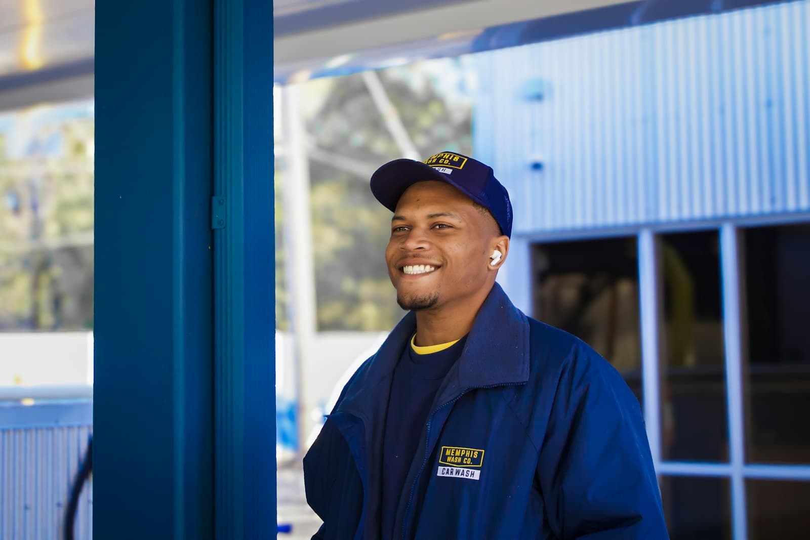 A smiling service technician in a blue uniform and cap