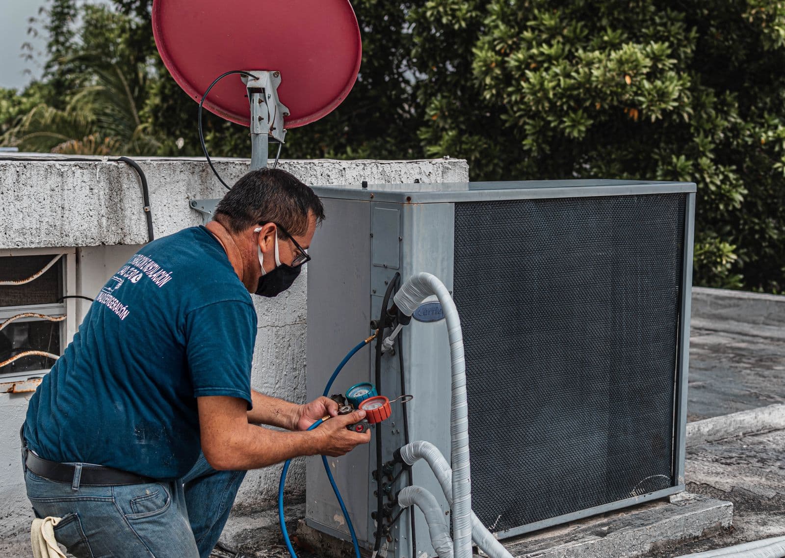 An HVAC technician checking refrigerant pressure with a manifold gauge on an outdoor air conditioning unit